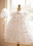 A vintage style white lace dress with ruffles and floral embroidery, complete with a bonnet and bloomers.